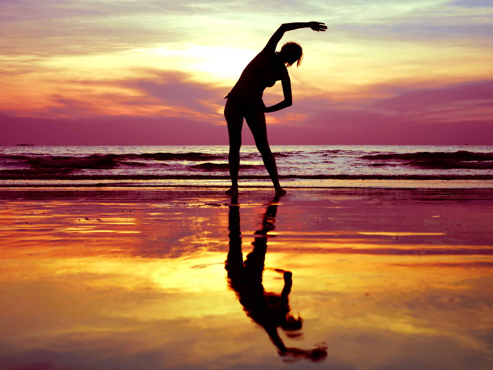Immagine di donna che fa stretching sulla spiaggia al tramonto i colori caldi del mare e del cielo che si fondono insieme